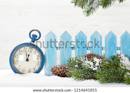 Christmas alarm clock and fir tree branch covered by snow in front of wooden wall. With copy space for your greetings
