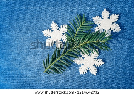 A green fir twig with snowflakes on blue jeans denim background simple Christmas decoration