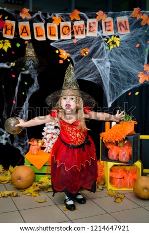A child, a little girl in the shape of a witch on a broomstick, poses against the backdrop of scenery of cobwebs, pumpkins and autumn leaves on a Halloween holiday.