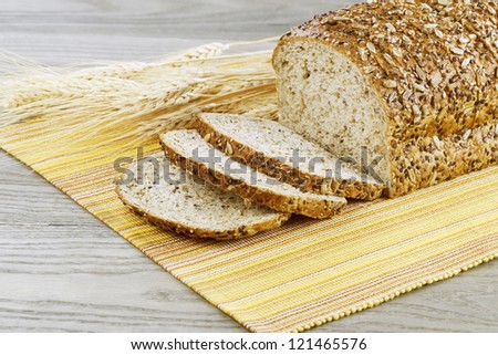 Fresh sliced whole bread with wheat stalks, yellow cloth place mat on faded wooden table