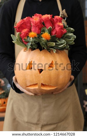 Beautiful flower arrangement of pumpkin and tomato color red roses for Halloween celebration in florist hands. Vertical. Close-up.