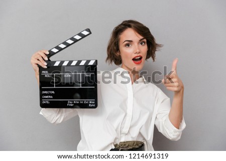 Photo of young woman 20s smiling and holding black clapperboard isolated over gray background