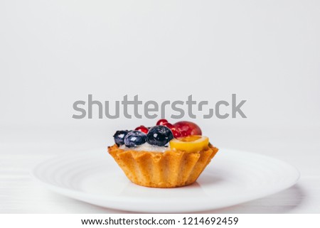 Close-up beautiful tartlet with berries on plate. Clean image elegant cupcake decorated with blueberries, currants and mango on white background with copy space.
