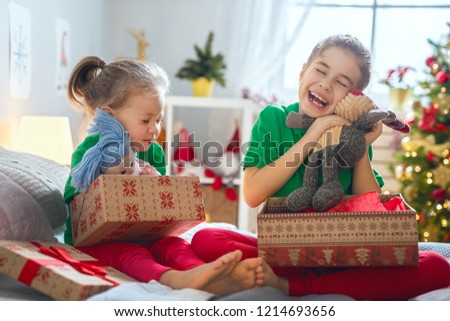 Merry Christmas and Happy Holidays! Cheerful cute childrens girls opening gifts on the bed. Kids wearing pajamas having fun near tree in the morning. Loving family with presents in room.