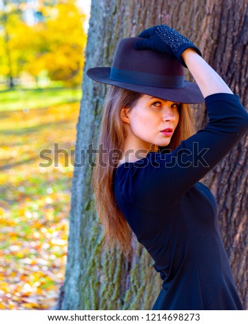 Beautiful happy smiling girl with long hair, red lips, wearing black hat, black jacket posing in autumn park. Outdoor portrait, 