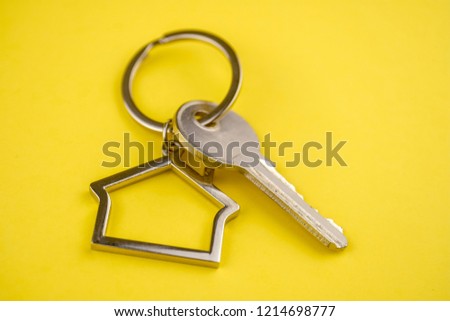 The concept of buying a private house or apartment. Metal keyring in the shape of a house with a metal key on a yellow background. Close up.