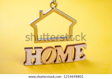 The concept of buying a private house or apartment. Metal keychain in the shape of a house with the word "home" of wooden letters on a yellow background. Close up.