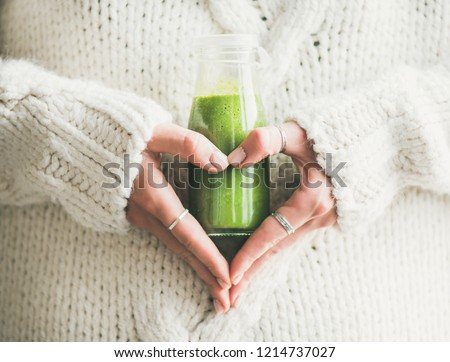 Winter seasonal smoothie drink detox. Female in woolen sweater holding bottle of green smoothie or juice making heart shape with her hands. Clean eating, weight loss, healthy dieting food concept Royalty-Free Stock Photo #1214737027