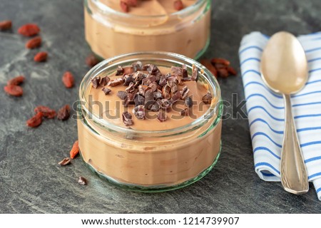 Whipped quark mousse with melted dark chocolate, cocoa nibs and goji berries.Perfect dieting desert or snack. On table. Natural light, selective focus. Warm, toned picture. 