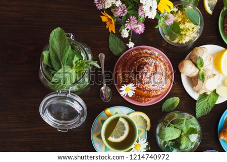Cup of herbal tea with lemon and mint leaves, ginger root and baked goods, on the wooden background 