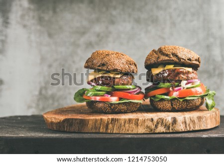 Beef meat cheeseburgers with barbeque sauce on rustic wooden board, grey concrete wall at background, copy space. Comfort food, burger bistro concept