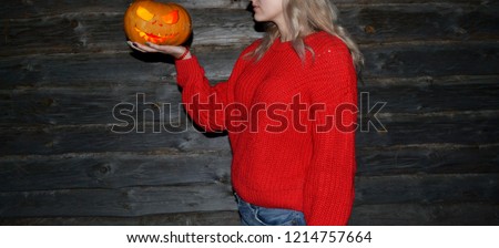 The girl in a red sweater holding Halloween pumpkin against the background of wooden logs. Carved Jack's lantern on the palm of a pretty young girl. Attractive woman
