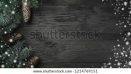 Christmas card. Black wood background with branches and fir cones in the side, top view. Xmas greeting card with snow effect. Royalty-Free Stock Photo #1214769151