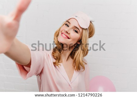 Close-up portrait of pleasant fair-haired girl enjoying morning. Indoor photo of smiling magnificent woman in eyemask taking picture of herself.