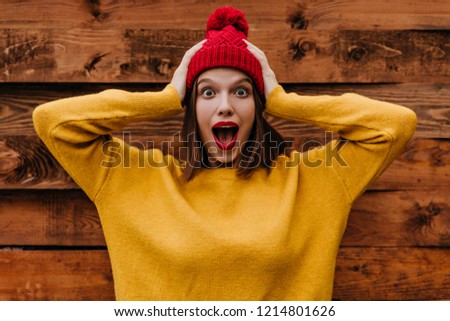 Amazed lovely girl touching her head on wooden background. Photo of emotional brunette woman wears trendy yellow sweater.