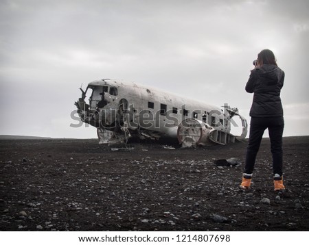 Girl is taking picture of abandoned crashed plane in Iceland in black sand desert