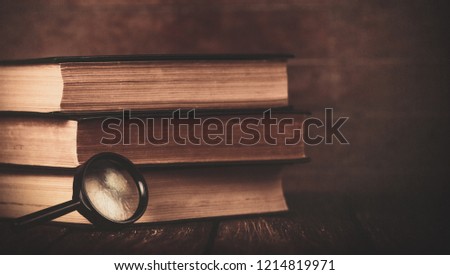 Books with loupe on wooden background. Photo in old color image style