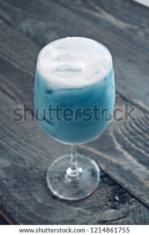 Selective focus of the frosty milk and ice cube in The butterfly pea flower tea in wine glass in brown wooden background, in Thai called " Nam dok anchan
