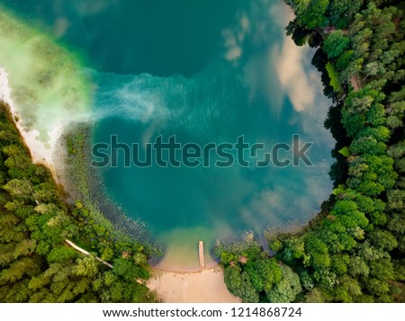 Aerial top down view of beautiful green waters of lake Gela. Birds eye view of scenic emerald lake surrounded by pine forests. Clouds reflecting in Gela lake, near Vilnius city, Lithuania. Royalty-Free Stock Photo #1214868724