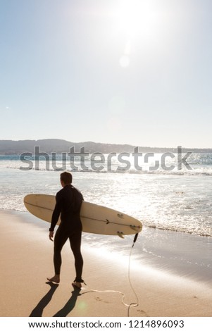After a long day of surfing a young man walks along the beach carrying his surfboard. 