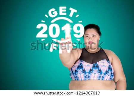 Picture of fat woman wearing sportswear while touching a virtual screen with text of get fit 2019