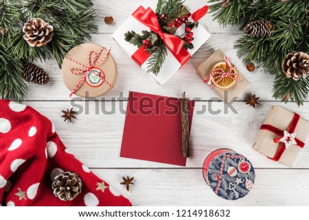 Creative layout frame made of Christmas tree branches, paper card note, pine cones, gifts, Christmas sweater on white wooden background. Xmas and New Year theme. Flat lay, top view