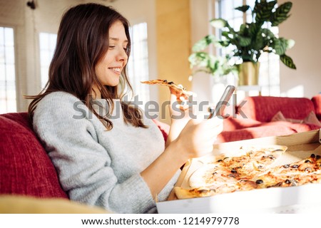 Portrait of handsome woman eating pizza at home and taking photo of her food to share memory