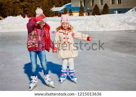 Little girls learn to skate. They are laughing and happy. Concept of friendship and fun holidays.