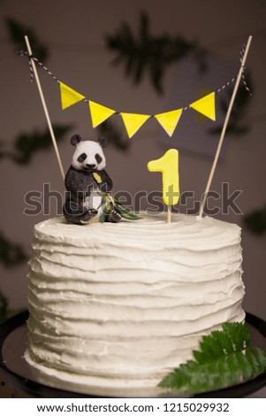 Closeup of a beautiful white birthday cake. Festive delicacy. Healthy carrot cake for 1-year-old child, decorated with a toy panda, a flag banner and fern leaves in the background. Idea of a holiday.