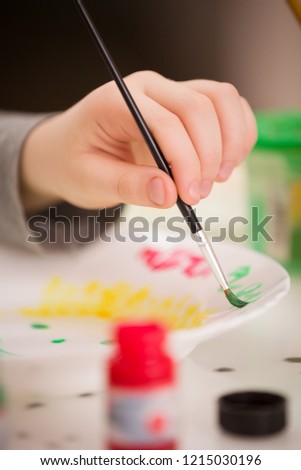 Little child sitting at the table and draws on the plate. After school. Education. A little boy creates a handmade gift.