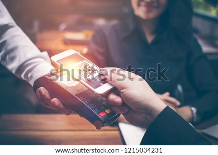 Young man hands are Smartphone to scan a QR CODE filing from a credit card reader to pay for food and beverages in restaurants which have a romantic atmosphere by the Asian girls are sitting together.