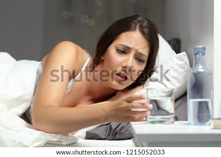 Thirsty woman reaching a glass of water lying on the bed in the night at home Royalty-Free Stock Photo #1215052033