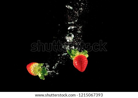 Fresh strawberry dropped into water with splash on isolated black background.