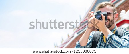 Male tourist photographer taking photo with camera while traveling in Bangkok Thailand with Thai temple in background, panoramic banner with copy space