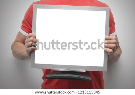 Man is holding a computer monitor with blank screen in front of him isolated on gray background.