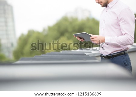 Attractive business man using tablet pc outside on the balcony with green trees in background