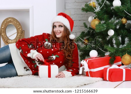 Smiling young woman opening a gift box near beautiful Christmas tree at home. Luxurious Christmas decoration. Presents for Christmas and New Year.