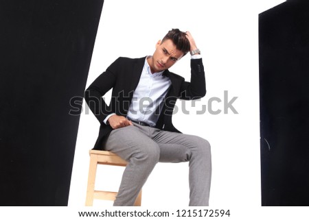 surprised businessman sits on chair and looks down to side while holding his head, portrait picture