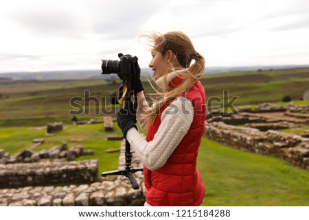 Professional photographer taking pictures outdoors. Cloudy autumn weather. Beautiful nature around. Ancient stone ruins on the background.