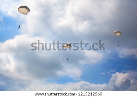 Three paratroopers jump with parachutes on the blue sky with white clouds background