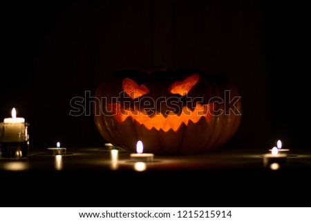 Glowing pumpkin for Halloween stands on the table near the candles