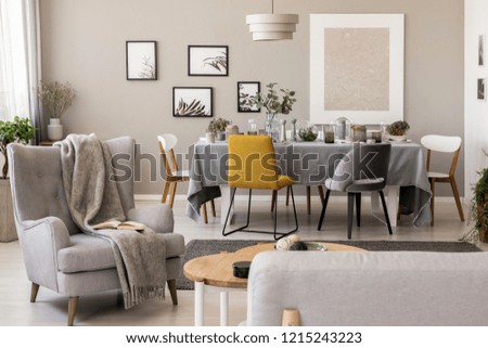 Blanket on grey armchair in spacious dining room interior with chairs at table. Real photo