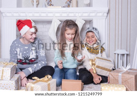 Group of three children. Merry Christmas and Happy Holidays concept. Family holiday. New Year's picture of brothers and sister. Children opening a gift at home. Friends are interested and amazed. Xmas