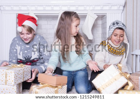 Group of three children. Merry Christmas and Happy Holidays concept. Family holiday. New Year's picture of brothers and sister. Children opening a gift at home. Friends are interested and amazed. Xmas
