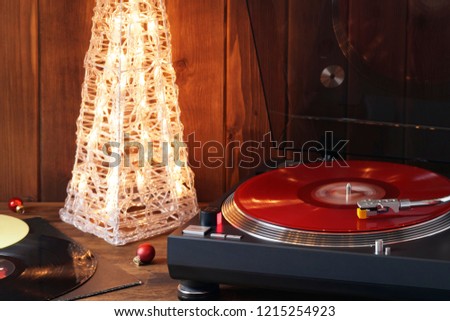 Christmas picture. The rotating moment of a red vinyl record on the turntable, the stylus with a needle falls on vinyl, music on the background of a glowing Christmas tree with red glass balls