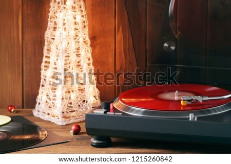 Christmas picture. The rotating moment of red vinyl record on turntable, stylus with needle falls on vinyl, music on the background of glowing Christmas tree with red glass balls. Noel. Front view