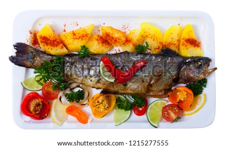 Picture of  tasty baked whole  trout  with potatoes, greens and tomatoes on white plate﻿. Isolated over white background

