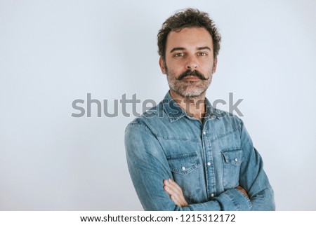 Portrait of brown, handsome man with mustache in jeans shirt standing with crossed arms. Gray background. Copy space Royalty-Free Stock Photo #1215312172