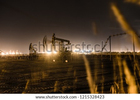 Working oil pump jack at night time. Oilfield during winter. Refinery lights background. Oil and gas concept. Toned.