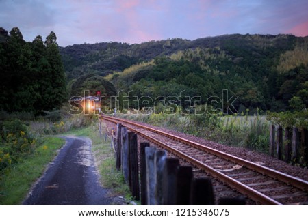 Train comes around bend in track under beautiful sunset sky in rural Japan